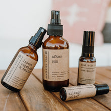 Load image into Gallery viewer, Group shot of natural products on a wood table outside. Products include after sun, bug spray, allergy relief essential oil roller and sore muscle rub