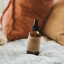 Load image into Gallery viewer, Relaxing pillow mist spray in an amber glass bottle on a bed with burnt orange pillows.
