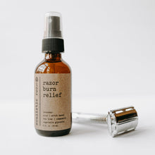 Load image into Gallery viewer, Razor burn relief after shave spray in a 2 oz glass amber bottle next to a straight razor with a white background.