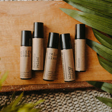 Load image into Gallery viewer, Essential oil rollers. There are five different blends -uplift which has rose quartz gemstones, headache relief, relax blend which has amethyst gemstones, allergy relief and breathe. They are in amber roller bottles on a wood block in next to a palm leaf.