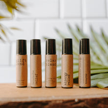 Load image into Gallery viewer, Essential oil rollers. There are five different blends -uplift which has rose quartz gemstones, headache relief, relax blend which has amethyst gemstones, allergy relief and breathe. They are in amber roller bottles on a wood block in front of a palm leaf.