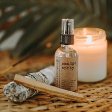 Load image into Gallery viewer, Amethyst Infused Essential Oil Smudge Spray on a wicker table with a sage and palo santo burning. There is also a white candle and palm leaf.
