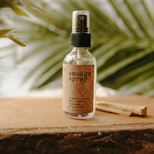 Load image into Gallery viewer, Amethyst Infused Essential Oil Smudge Spray next to a stick of palo santo on a wooden block. There is a palm tree in the background.
