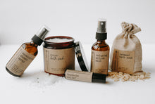 Load image into Gallery viewer, The spa gift set which includes a eucalyptus shower spray, organic lavender oatmeal bath soak, headache relief roller, essential oil &amp; herb revive bath soak and a relaxing pillow mist. The set is on a blanket in front of a white background with some of the oatmeal and epsom salt &amp; herbs spilt out.
