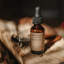 Load image into Gallery viewer, Beard oil in an amber bottle with glass dropper next to a silver straight razor on a wooden block. 
