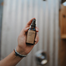 Load image into Gallery viewer, Essential oil based eucalyptus shower spray in a 2 oz amber glass bottle getting sprayed in an outdoor shower.
