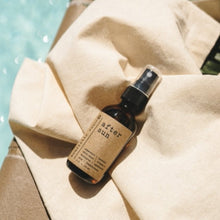 Load image into Gallery viewer, After Sun Aloe Vera Sunburn Spray 2 oz amber spray bottle on a towel next to the pool in the summer
