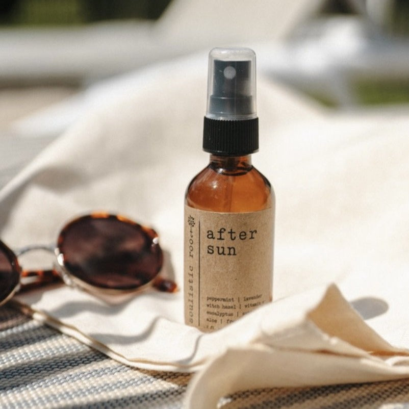 After Sun Aloe Vera Sunburn Spray 2 oz amber bottle sitting out by the pool next to a beach towel and a pair of sunglasses.