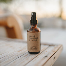 Load image into Gallery viewer, Bug spray that is an insect repellent and bug bite relief. 2 oz bottle on a wooden table outside in the summer
