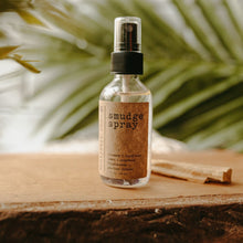 Load image into Gallery viewer, Amethyst Infused Essential Oil Smudge Spray next to a stick of palo santo on a wooden block. There is a palm tree in the background.
