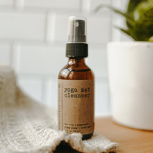 Load image into Gallery viewer, Yoga mat cleanser with rose quartz gemstones in a 2 oz glass amber bottle on a white blanket next to a plant in front of subway tiles.
