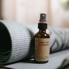 Load image into Gallery viewer, Yoga mat cleanser with rose quartz gemstones in a 2 oz glass amber bottle sitting on the floor in front of a roller up blue yoga mat.
